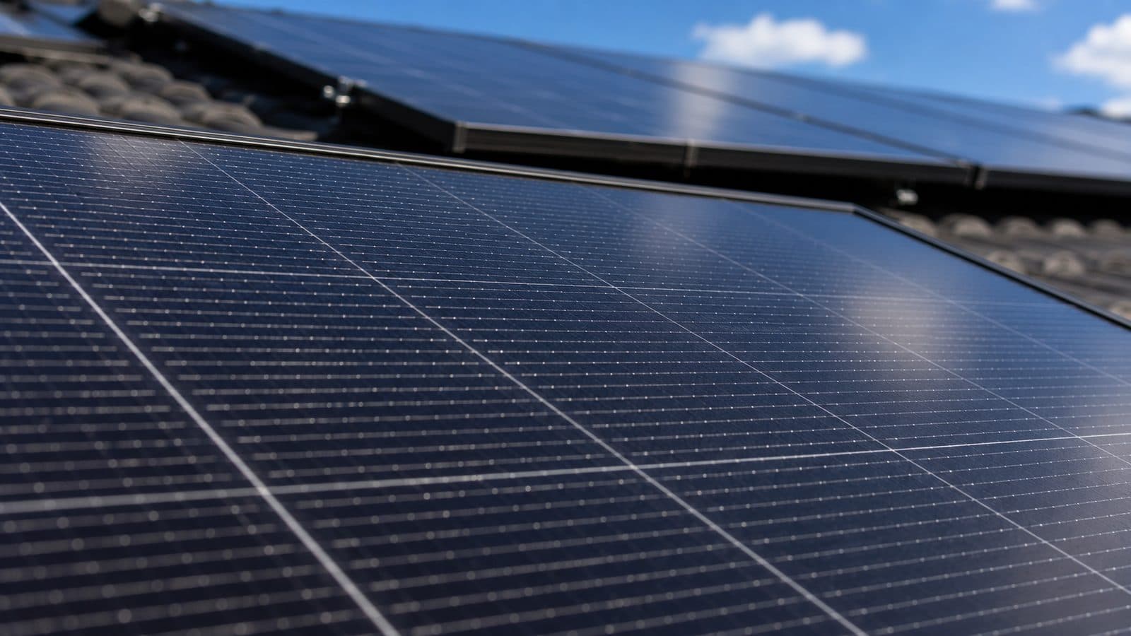 Close-up of black monocrystalline solar panels with visible silver busbar gridlines, installed on an Australian tile roof against a blue sky