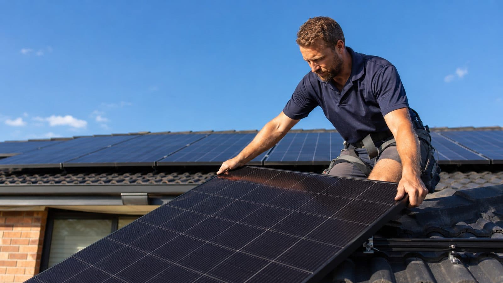 An Australian solar installer fitting a black monocrystalline panel onto a tile roof of a suburban home