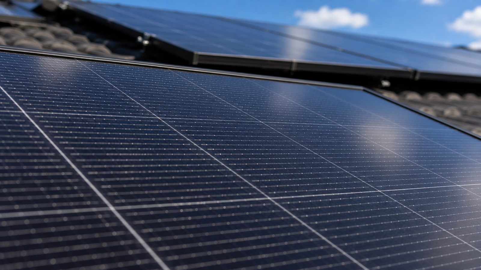 Close-up of black monocrystalline solar panels with visible silver busbar gridlines, installed on an Australian tile roof against a blue sky